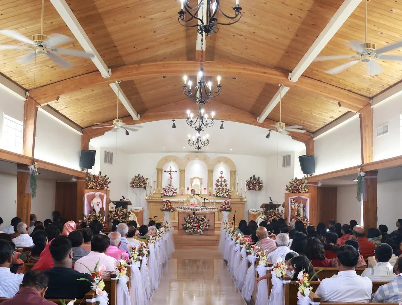 Church nave during Mass, priest at flower-covered altar, congregation in tulle-decorated pews