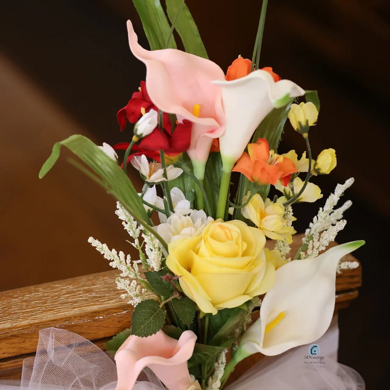 Close-up of a pew-end arrangement of calla lilies and a yellow rose tied with cream tulle to a wooden pew